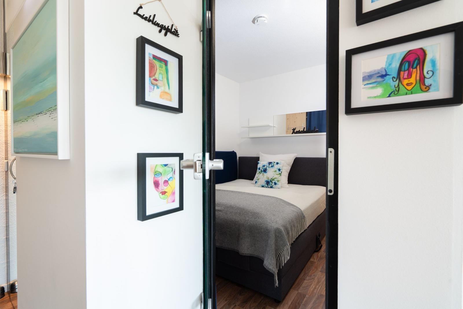 Bedroom with bed, wall art, and door. Room is well lit and modernly furnished.