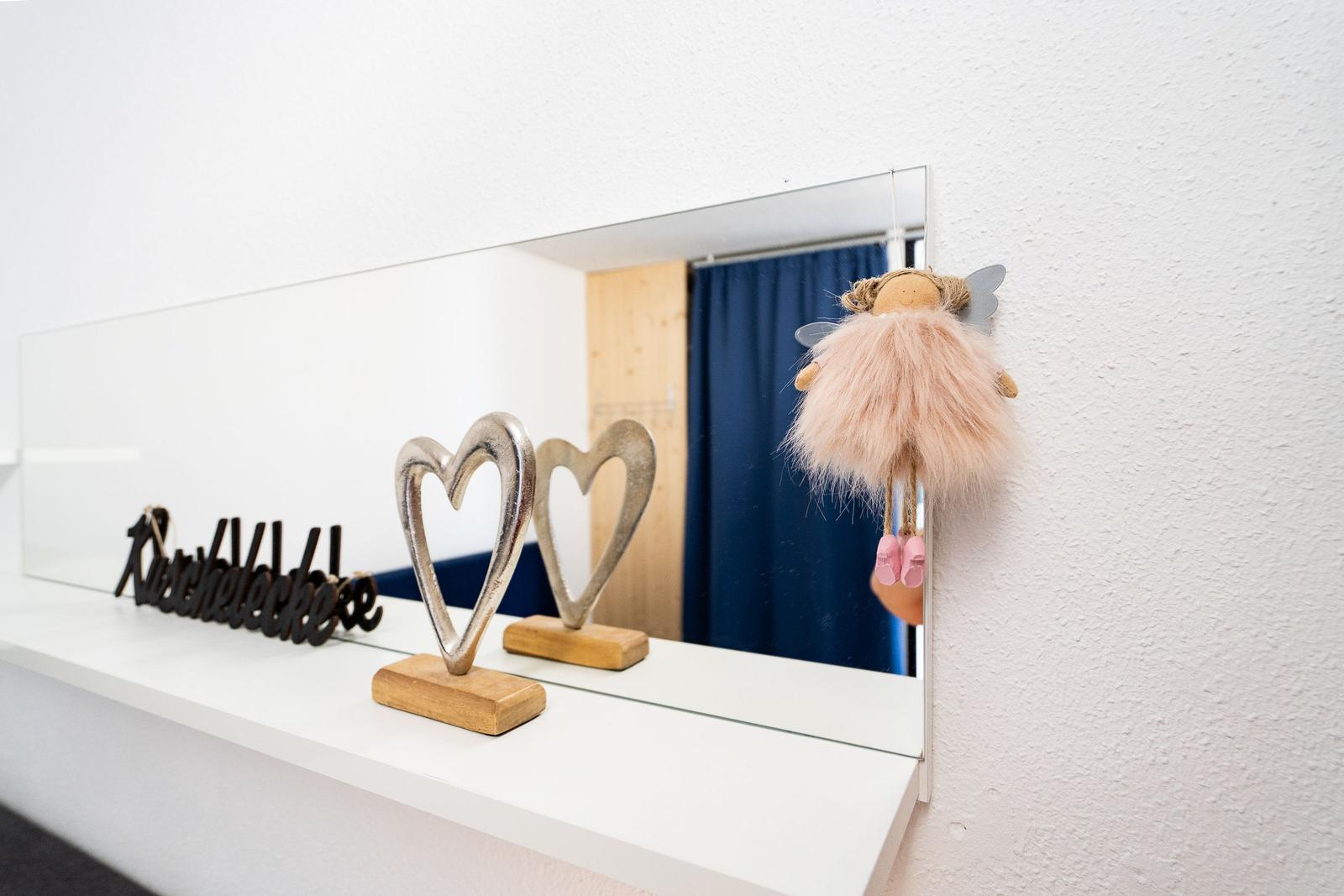 Mirror with heart figures and doll hanger on white shelf.