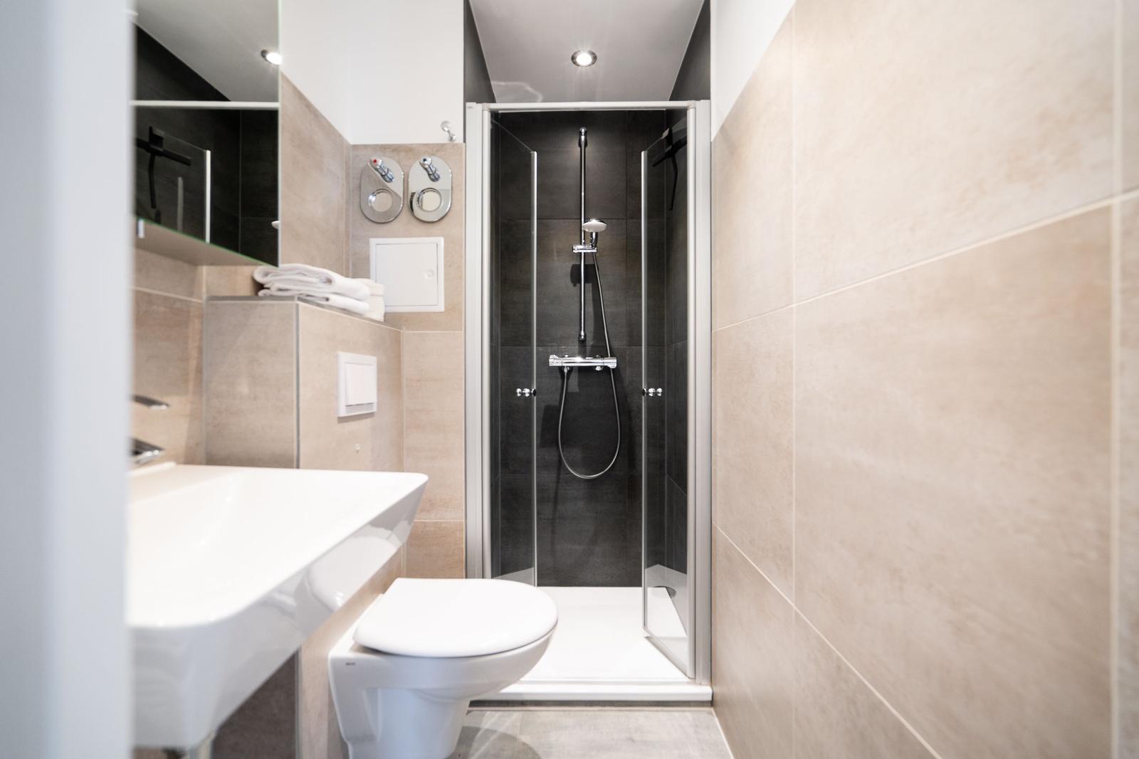 Bathroom with shower, sink, and toilet. Tiled wall and mirror visible.