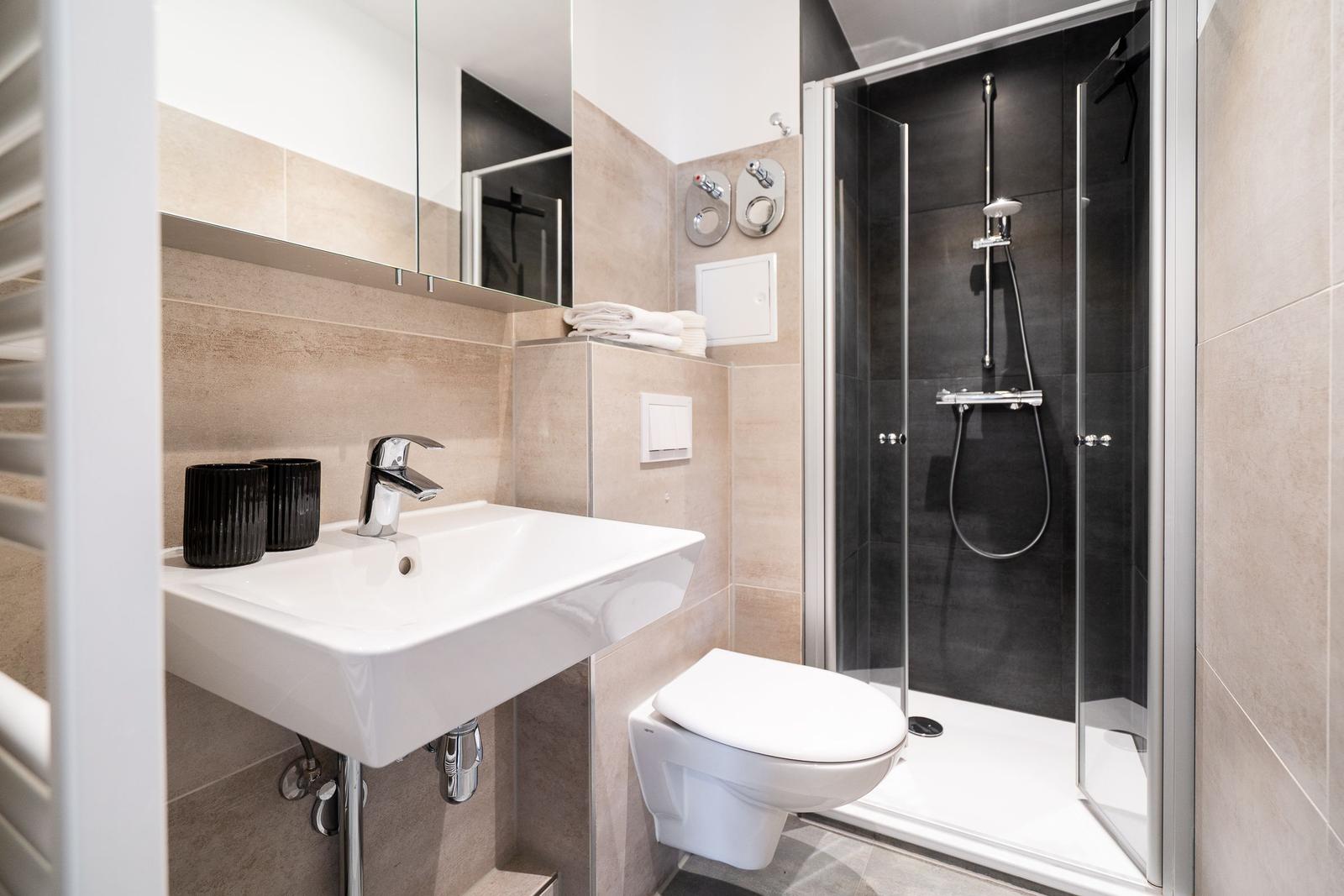 Bathroom with shower, sink, and toilet. Tiles in beige tones.