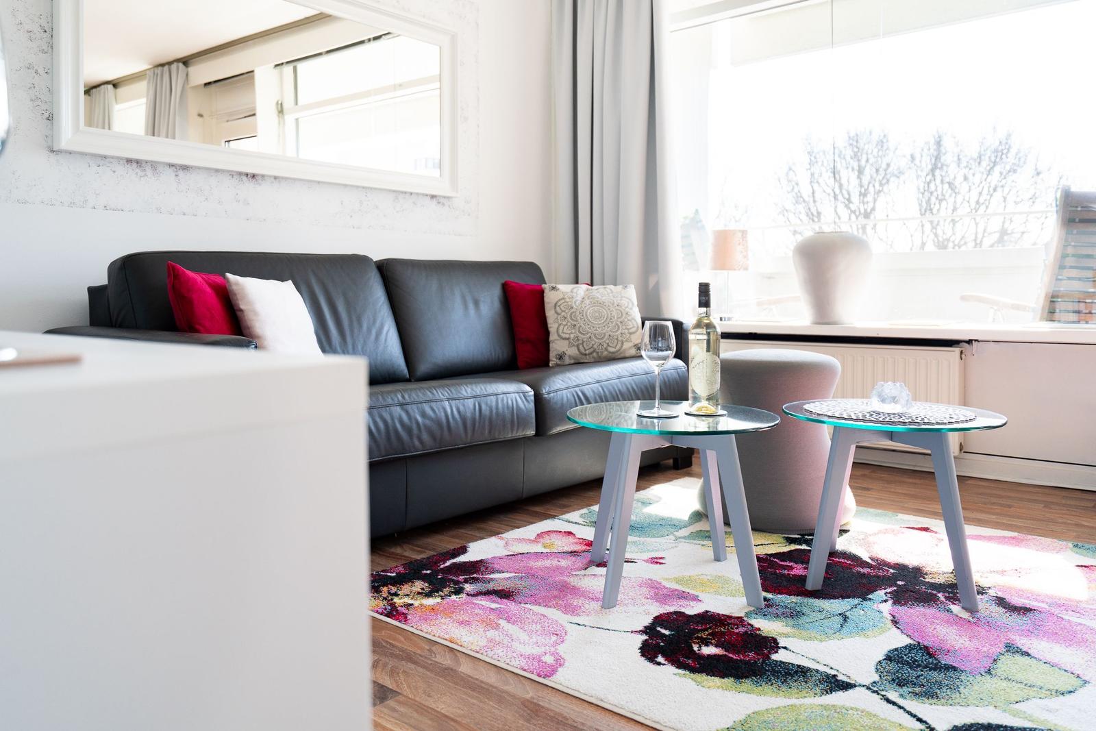 A living room with a black sofa, a colorful rug, and two glass tables.