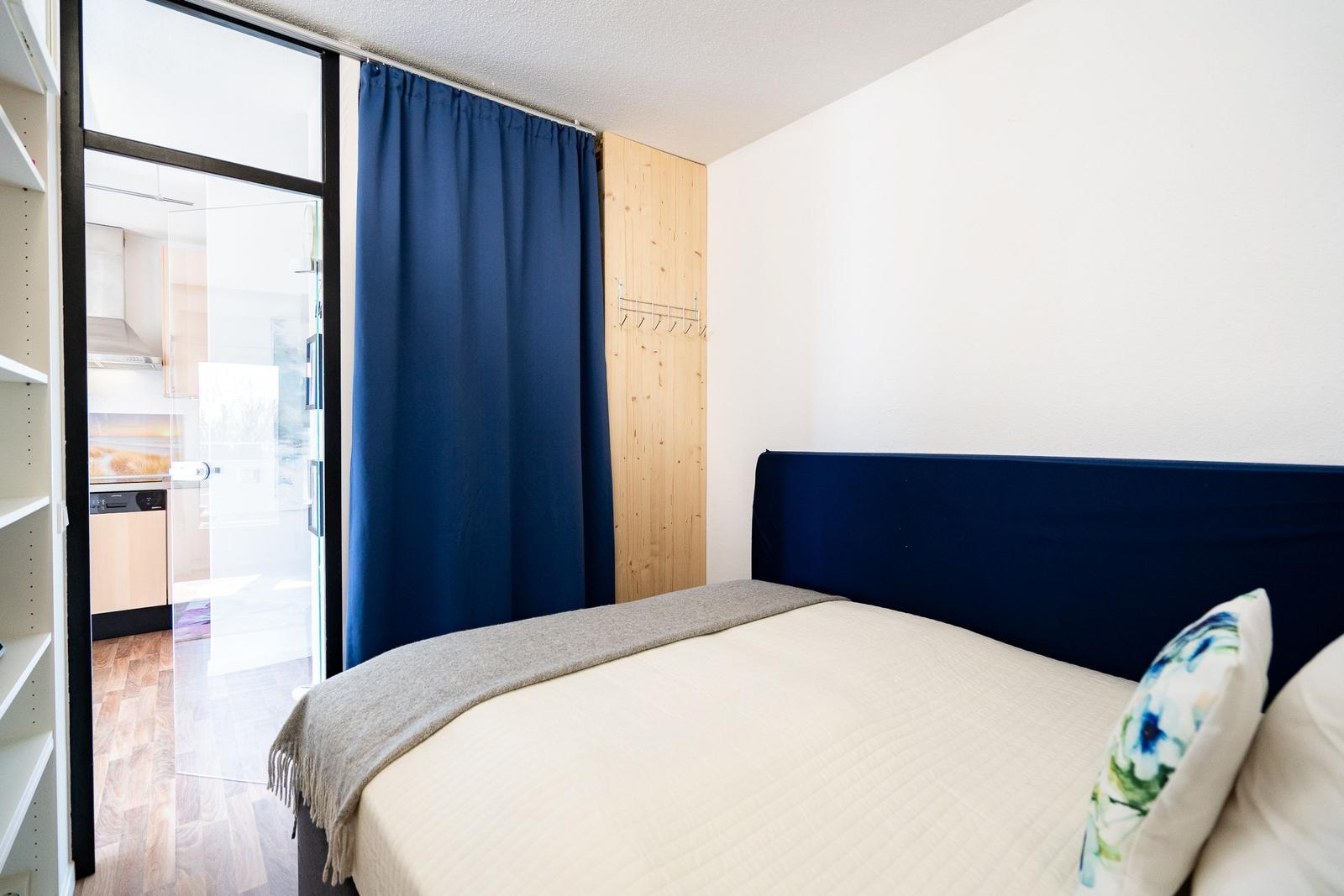 Bedroom with bed, blue headboard, and view into the kitchen.