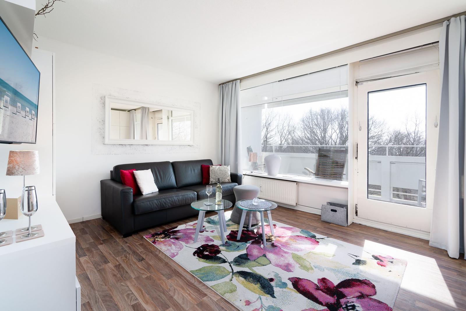 Living room with sofa, TV, and balcony door. Floral rug and large window.