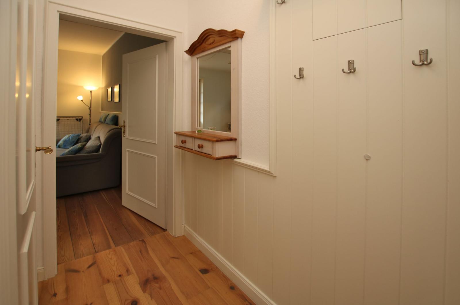 Flur mit Spiegelschrank, Garderobe und Blick in Schlafzimmer mit Sofa.