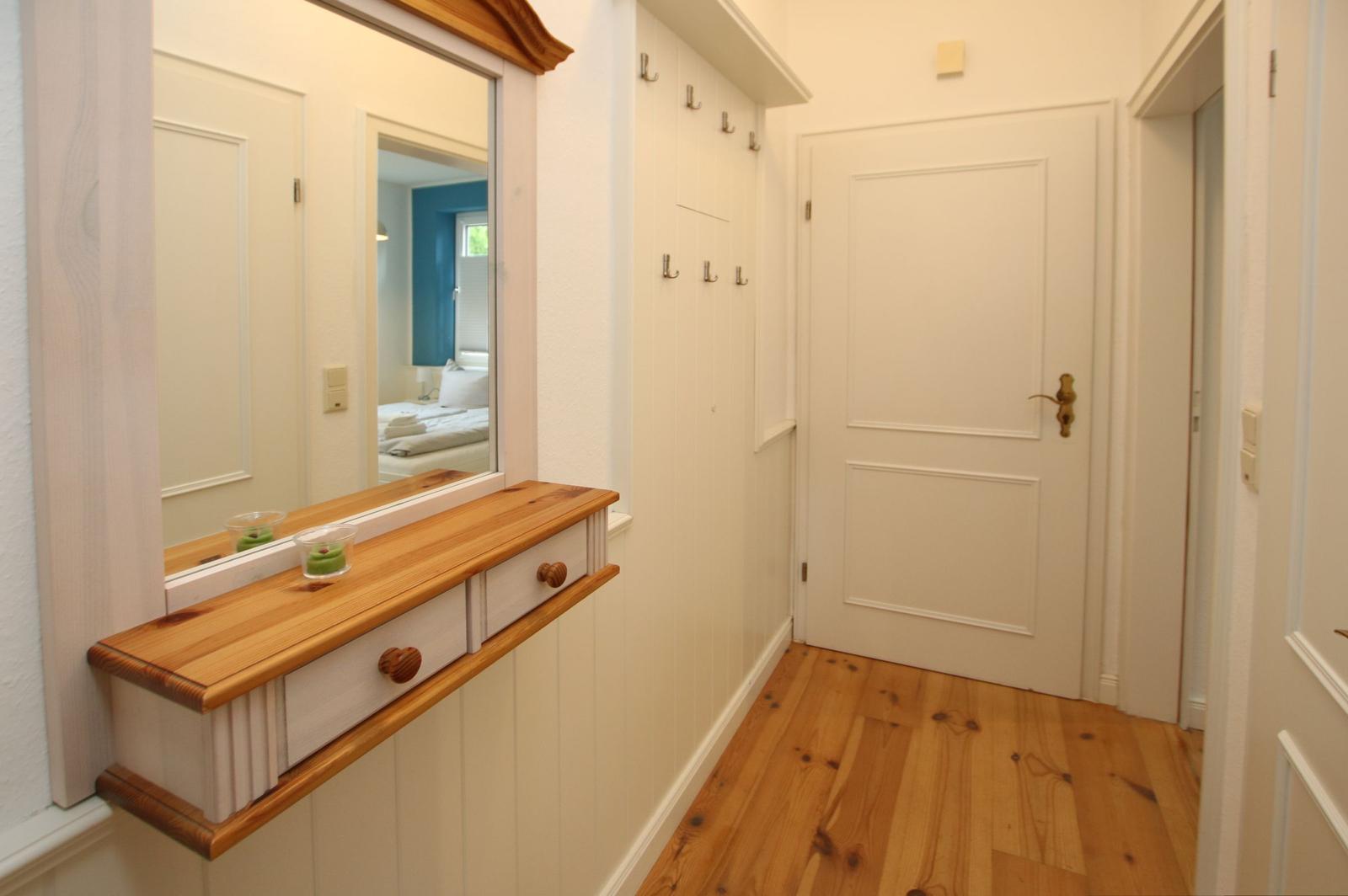 Flur mit Spiegel, Holzregal und Garderobe. Holzboden und weiße Türen.