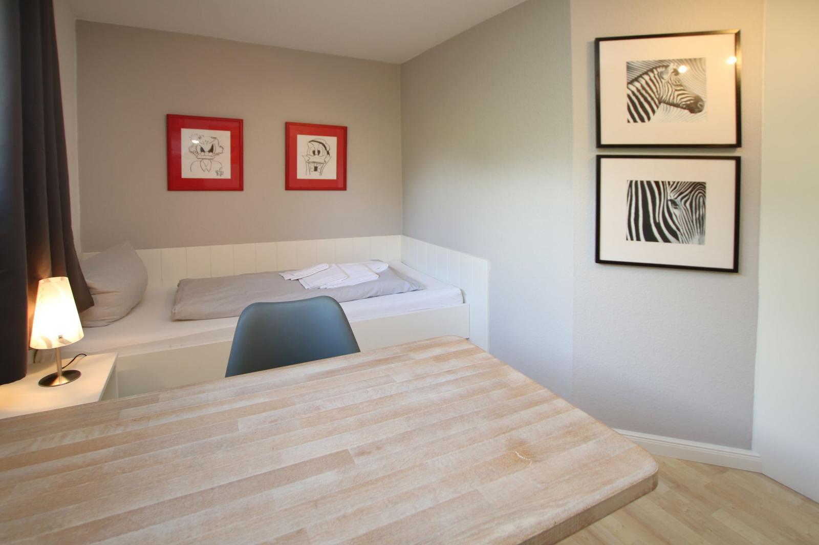Schlafzimmer mit Bett, Tisch und Wandbildern.