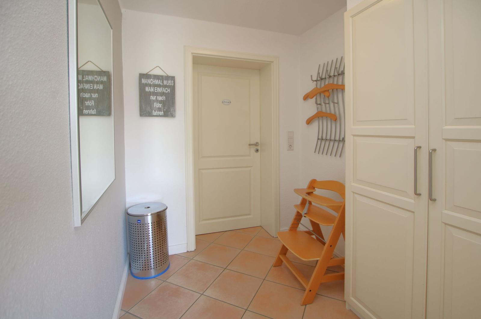 Eingangsbereich mit Kleiderständer, Kinderhochstuhl und Spiegel an der Wand.