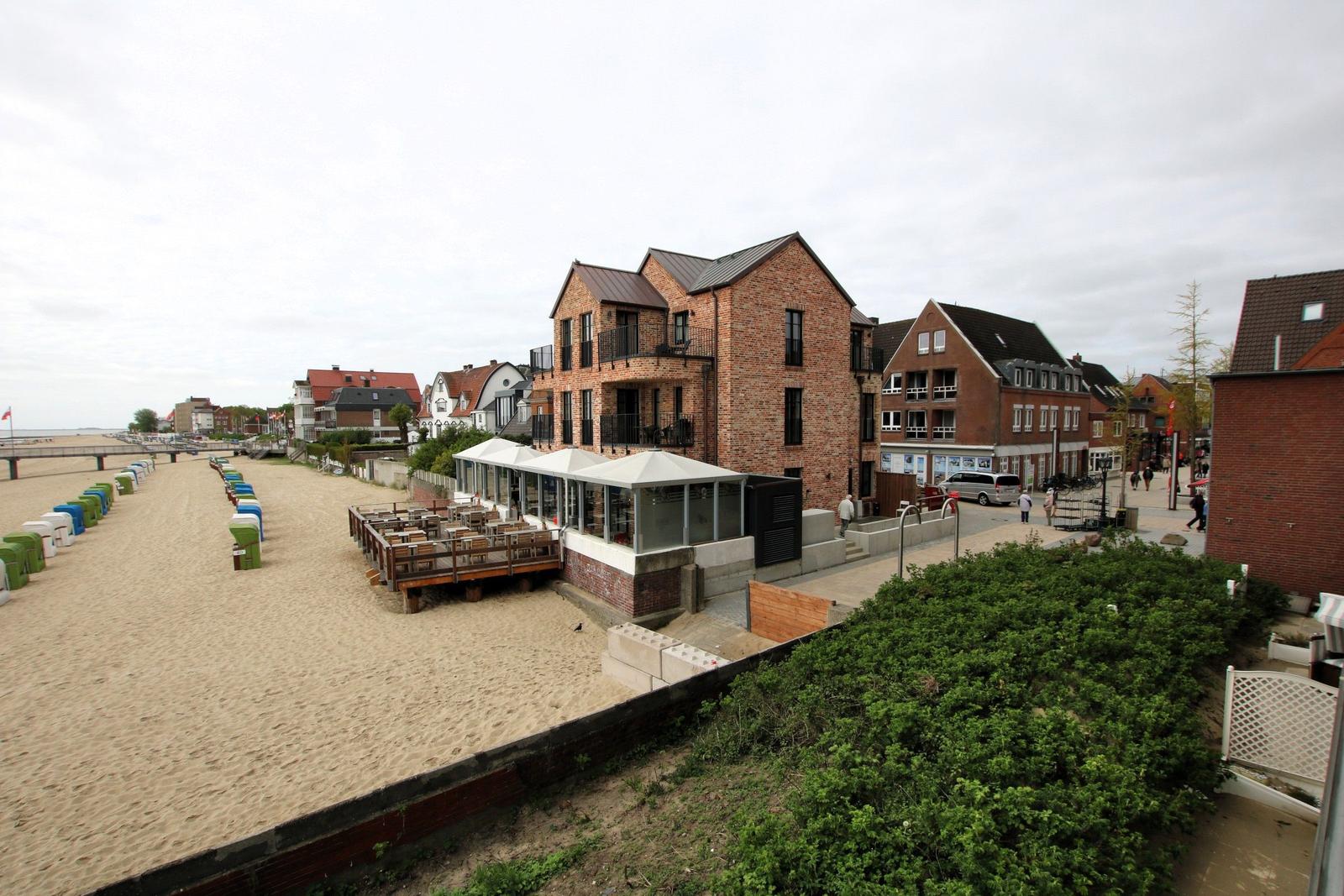 Strandfronthaus mit Terrasse und Blick auf den Sandstrand mit bunten Strandkörben.