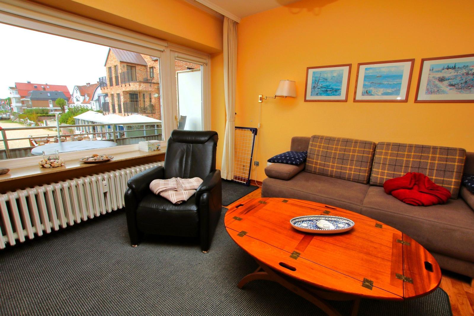 Wohnzimmer mit Sofa, Sessel und Tisch. Fenster mit Blick auf Strand.