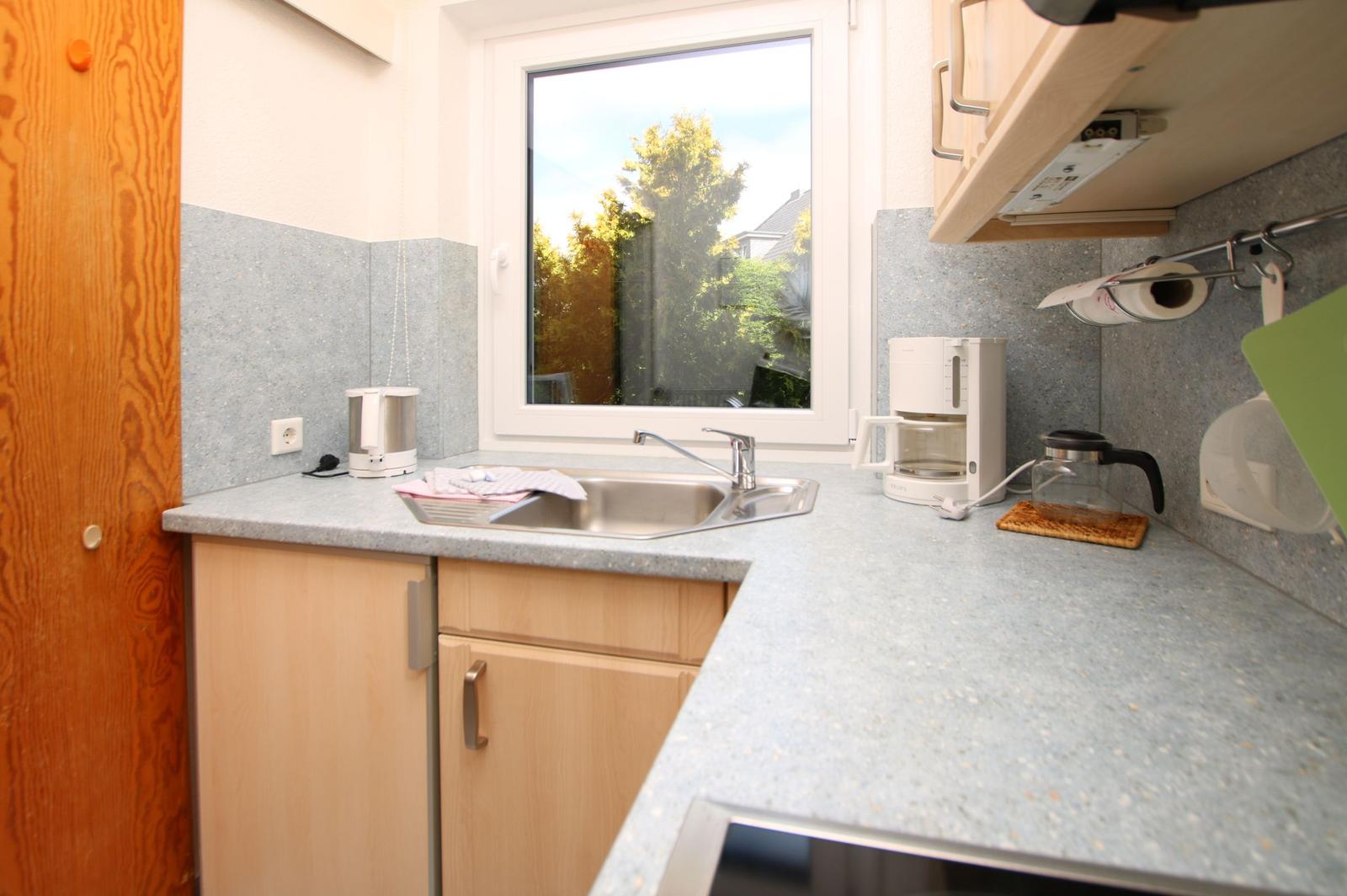 Küche mit Arbeitsfläche, Spüle und Fenster. Küchengeräte und -utensilien sind vorhanden.