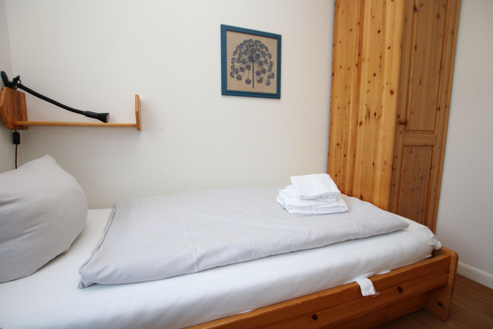 Ein Bett mit weißer Bettwäsche, einem Kissen und gefalteten Handtüchern. Holzgestell und Wandbild.