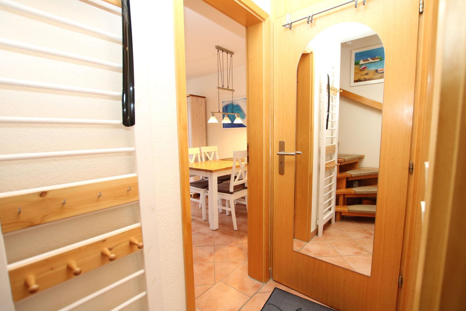 Entrance with wooden coat rack, view into dining room and stairwell with mirrored door.