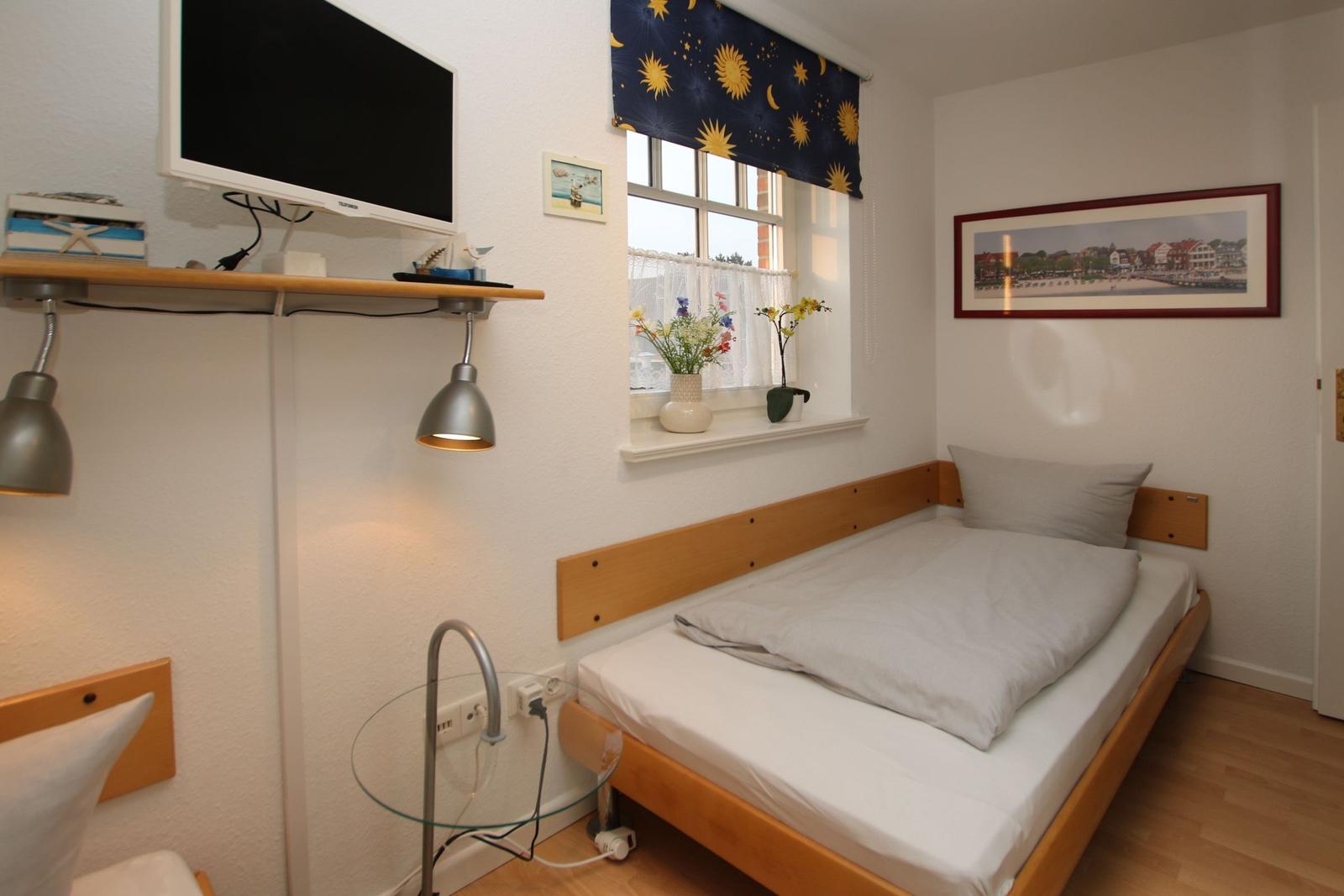 Ein Schlafzimmer mit einem Bett, einem Fenster und einer Wand-TV-Anlage.