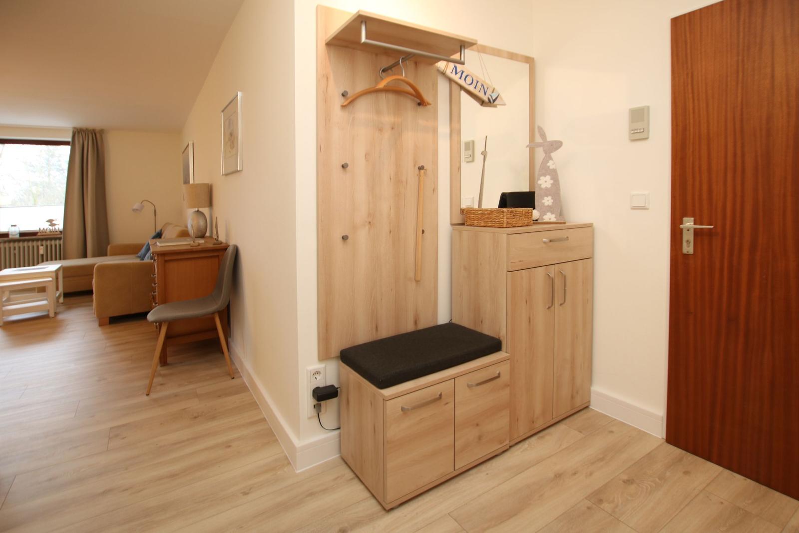 Eingangsbereich mit Kleiderständer, Schuhschrank und Sitzbank. Wohnzimmer im Hintergrund.
