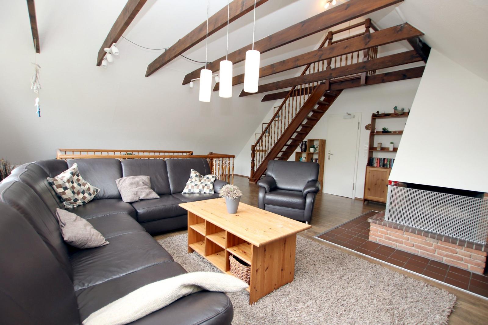 Wohnzimmer mit Sofa, Sessel, Holztisch und Kamin. Holzstufen führen zur Galerie.