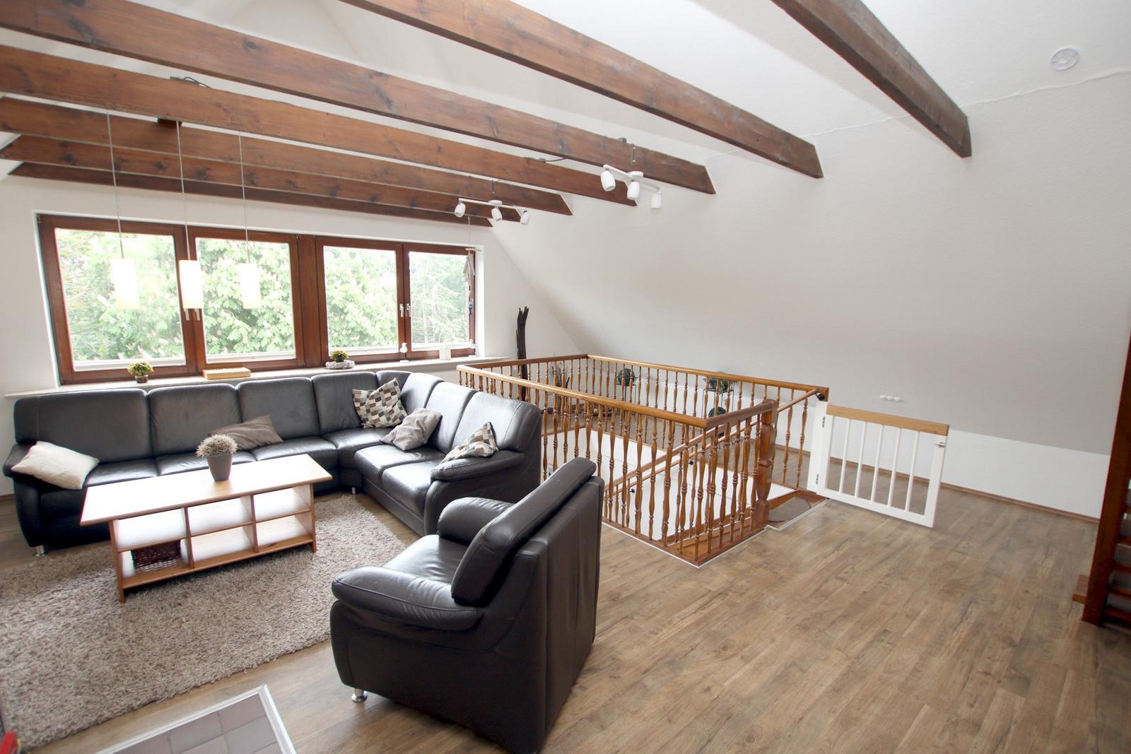 Wohnraum mit braunem Holzboden, dunklem Sofa und Holzgeländer.