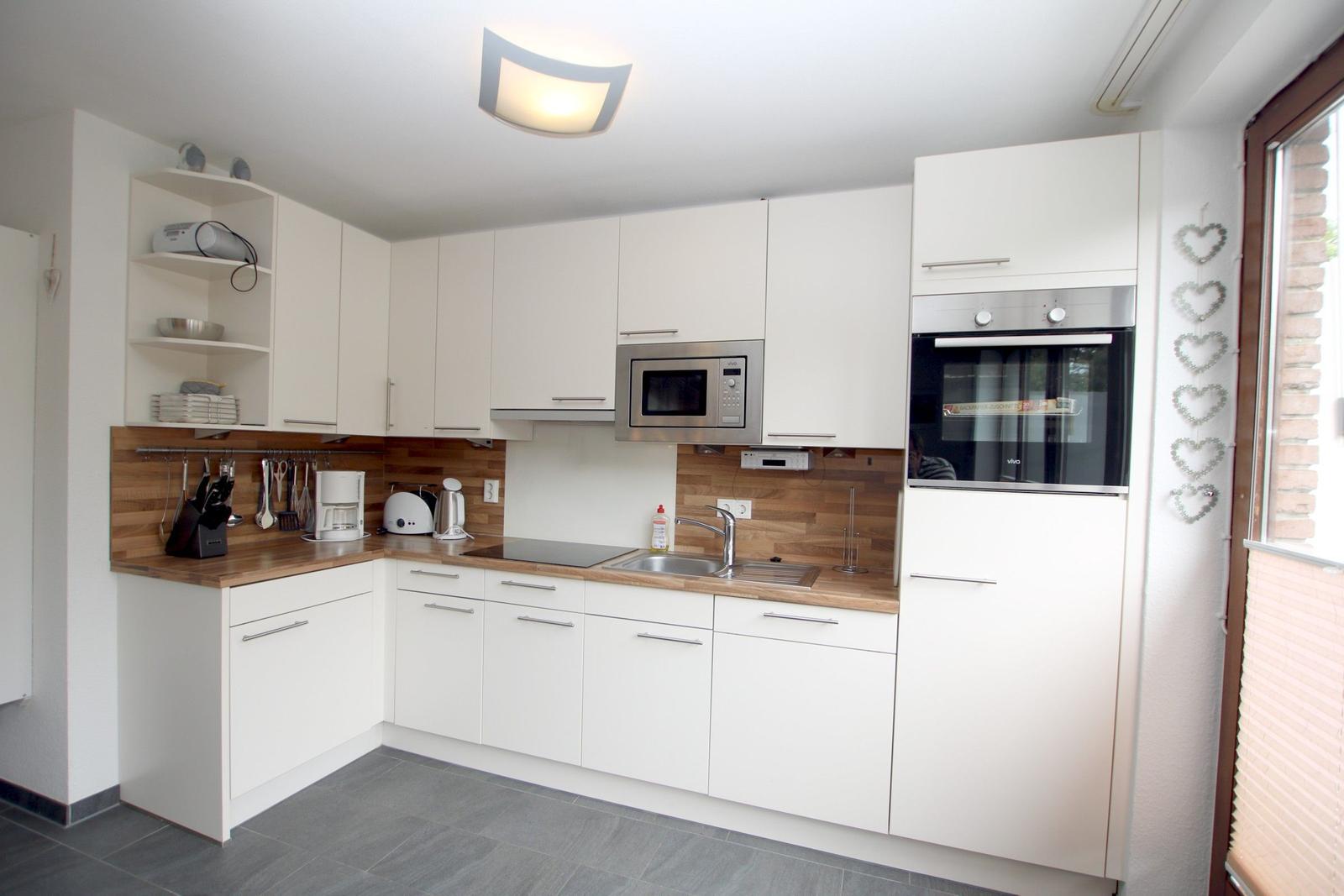 Küche mit weißen Schränken, Holzoberfläche und eingebauter Mikrowelle und Backofen.