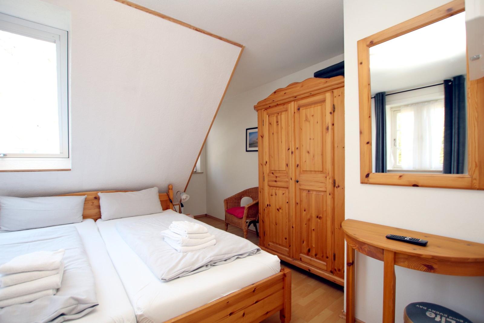Schlafzimmer mit Doppelbett, Holzschrank und Spiegel an der Wand.