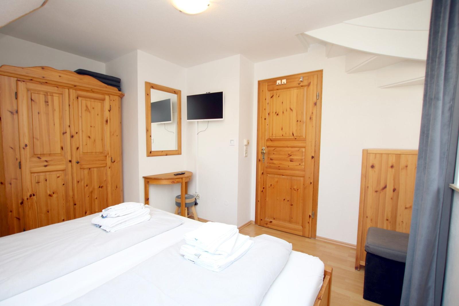Schlafzimmer mit Holzmöbeln, Bett, Fernseher und Tür.