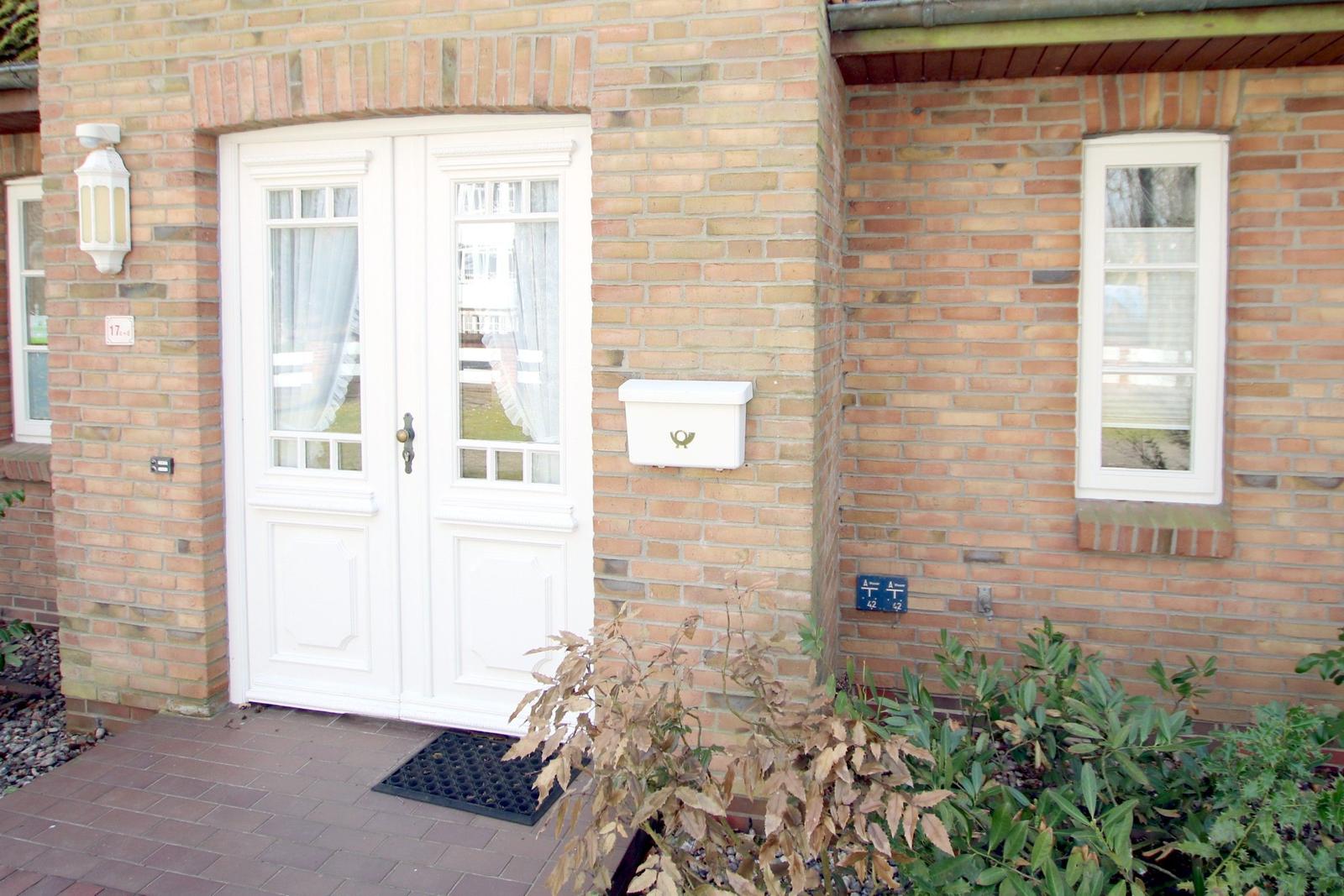 Haus mit weißen Türen und Fenstern, rotem Ziegelstein und Briefkasten an der Wand.