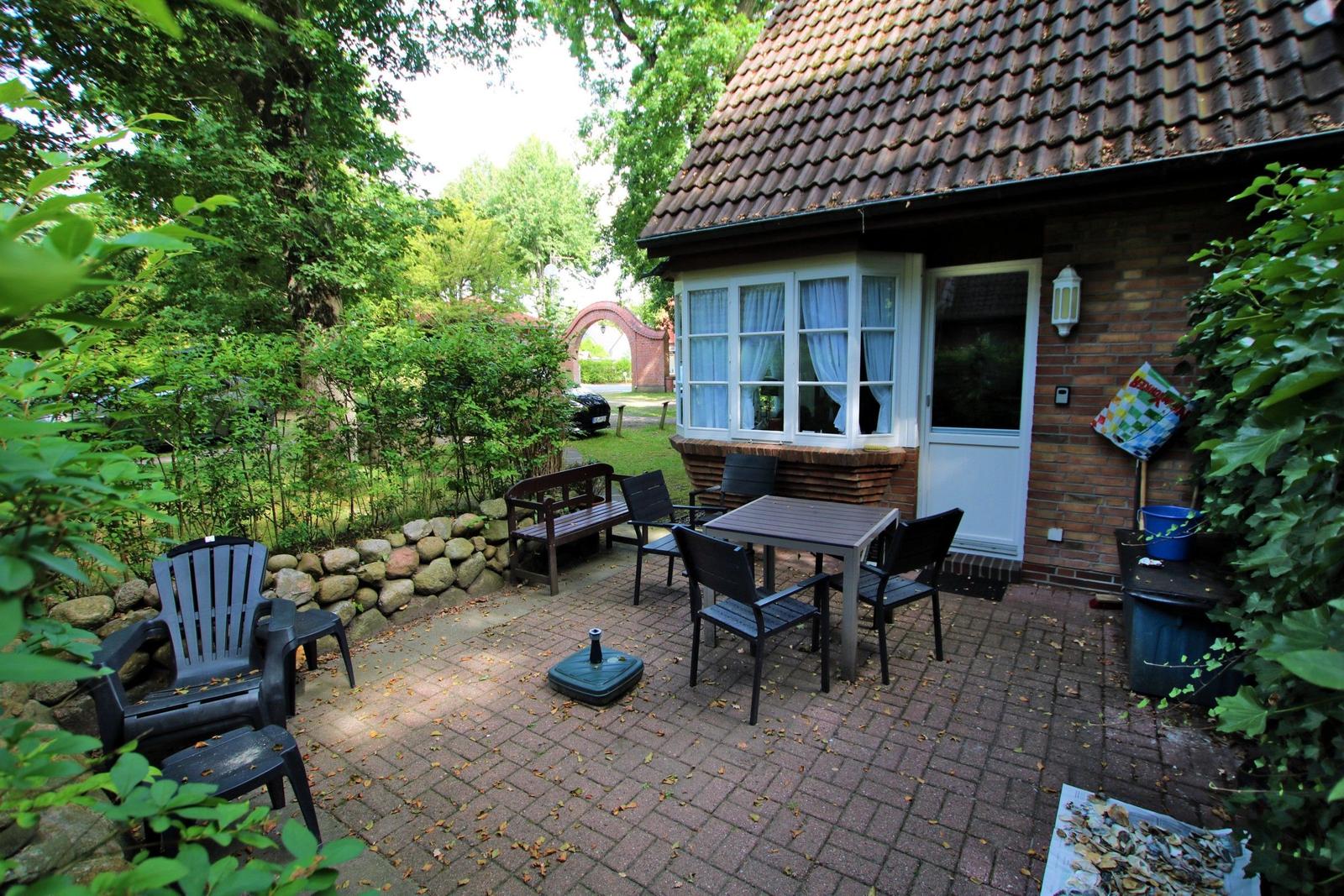 Terrasse mit Tisch, Stühlen und Gartenhaus. Umgeben von Bäumen und Sträuchern.