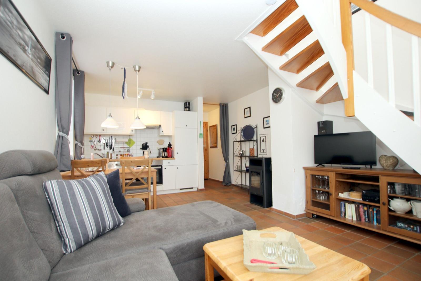 Wohn- und Küchenbereich mit Sofa, TV und Holztreppe.