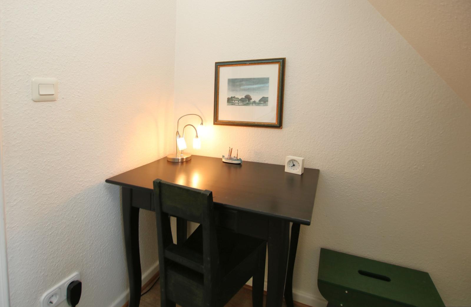 Desk with chair, lamp, clock, and picture on the wall.