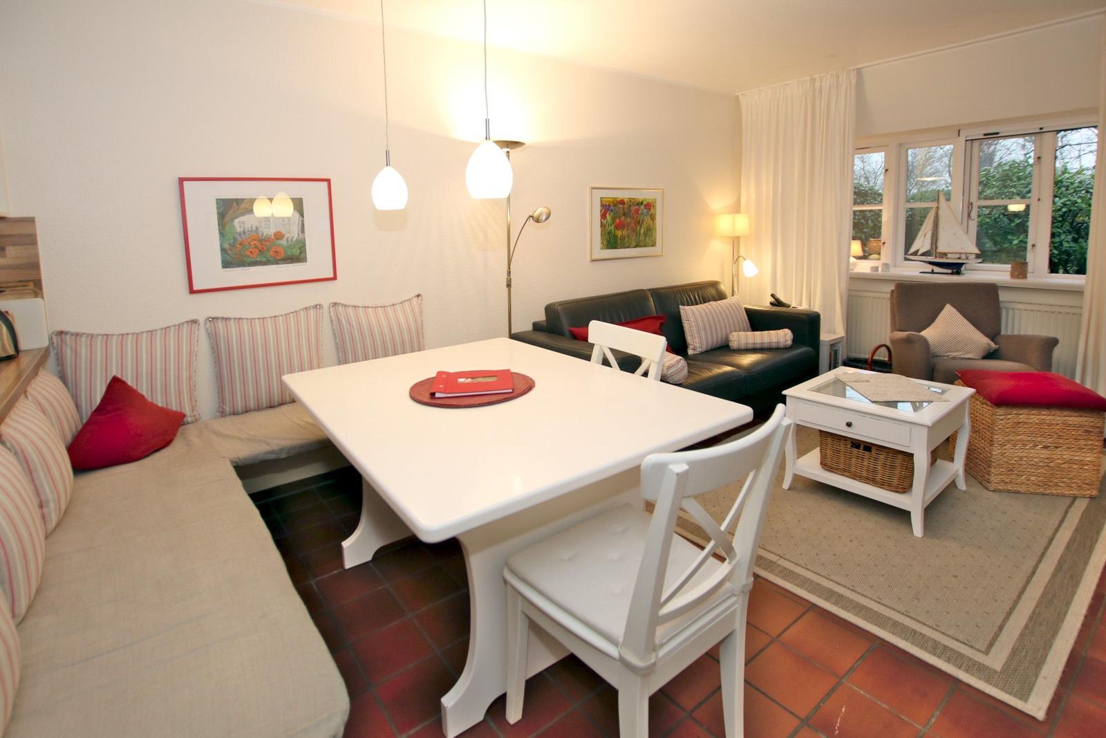 Living and dining area with white table, sofa, and window overlooking garden.