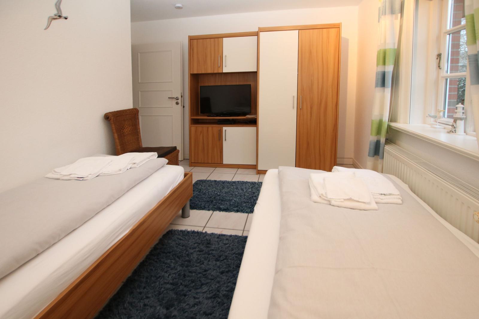 Zwei Betten, Kleiderschrank mit TV, Fenster mit Vorhängen.