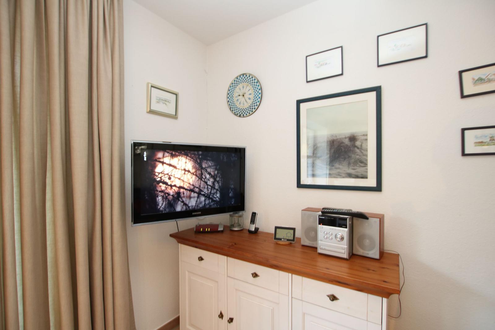 TV auf Holzschrank, Wanduhr und Bilder an der Wand