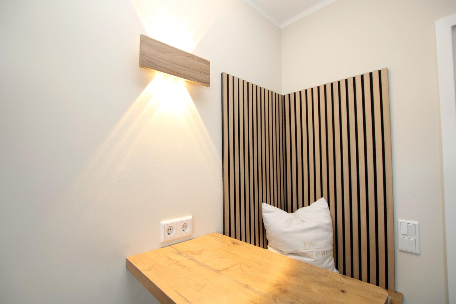Ein kleiner Schreibtisch mit Holzplatte und Wandbeleuchtung neben einem Sitzbereich mit Holzpaneelen.