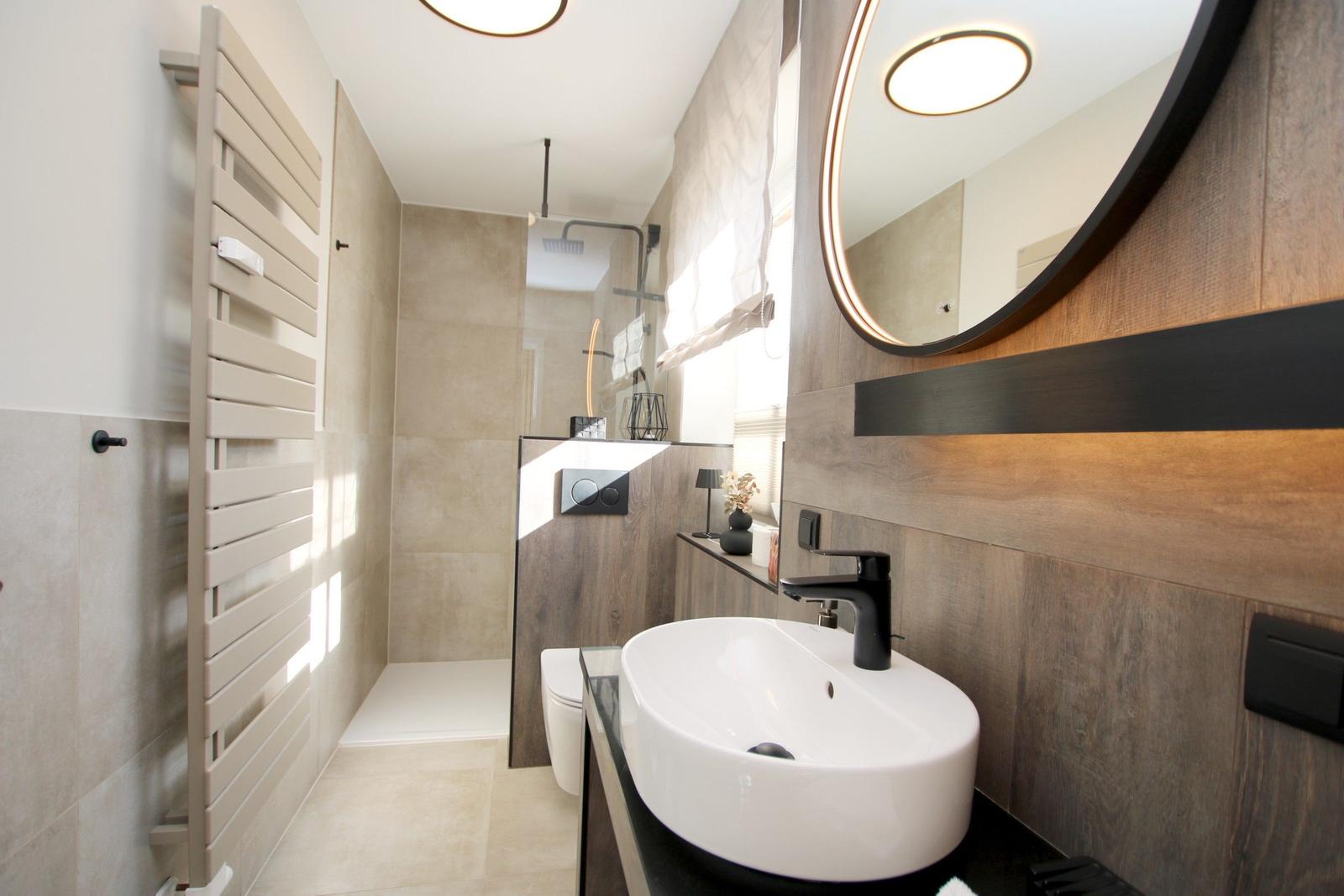 Badezimmer mit Waschbecken, Spiegel, Dusche und Heizkörper.