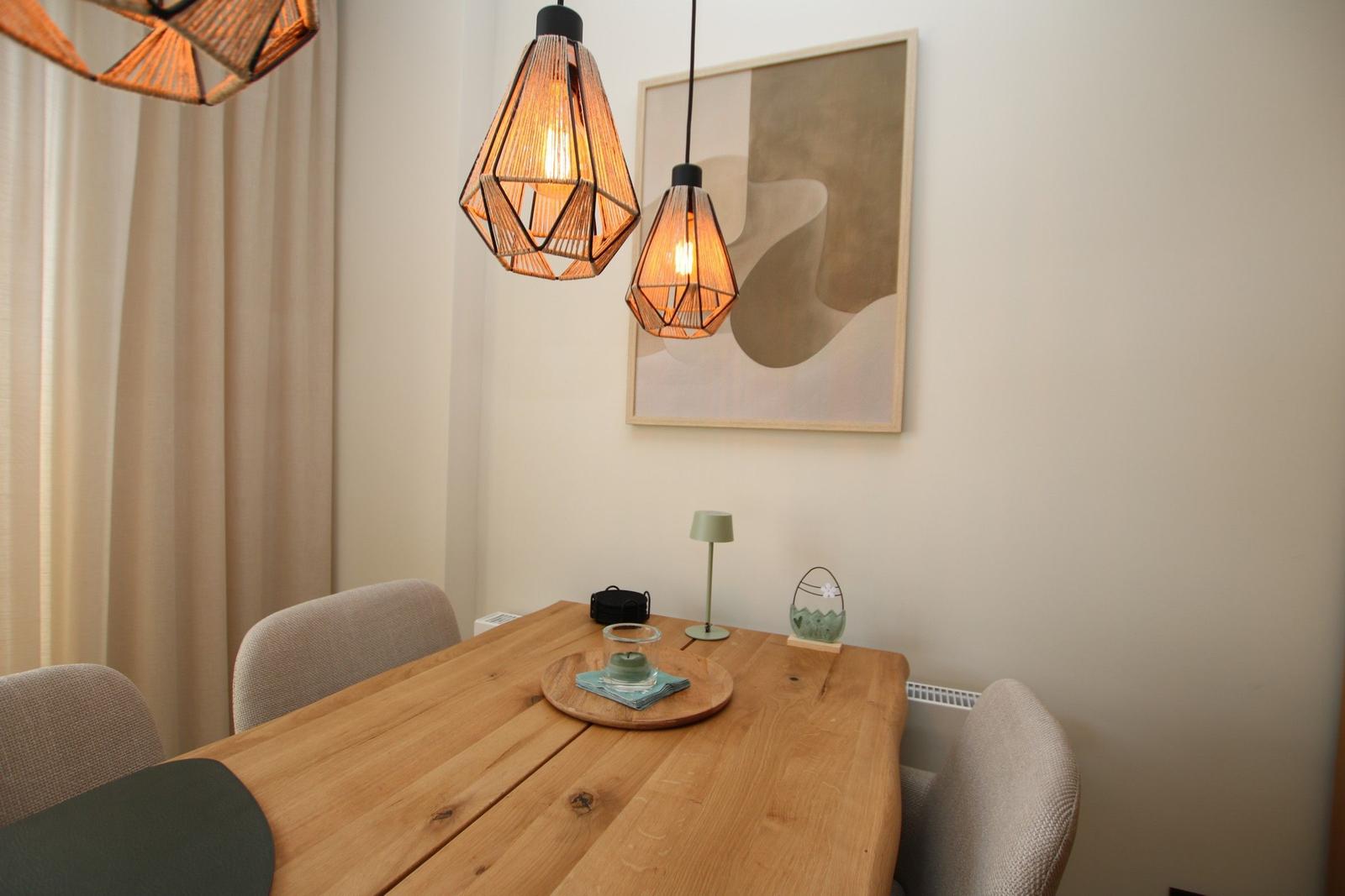 Holztisch mit Stühlen, zwei Hängelampen und Wandbild.