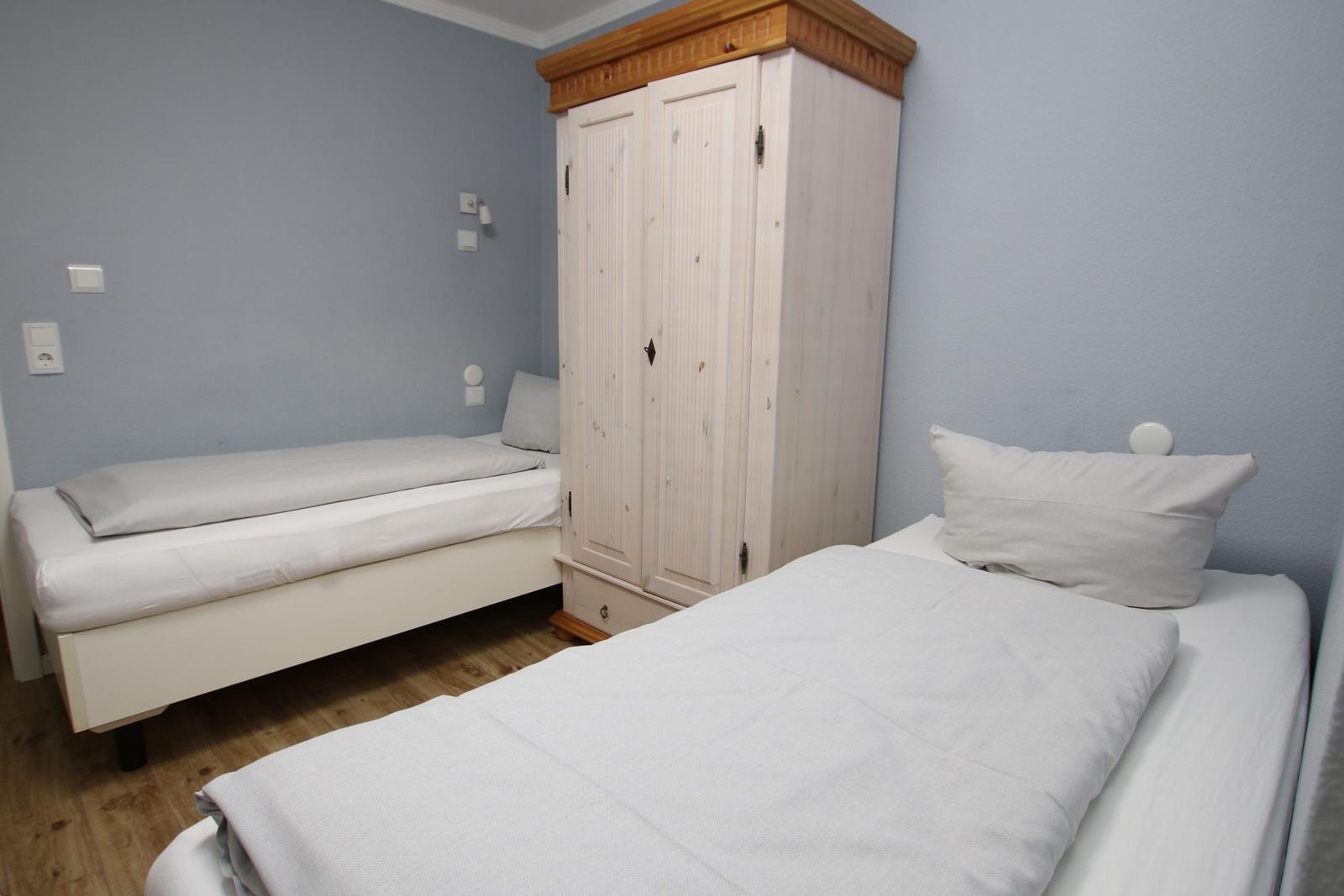 Zwei Einzelbetten und ein Kleiderschrank in einem Schlafzimmer mit hellblauen Wänden.