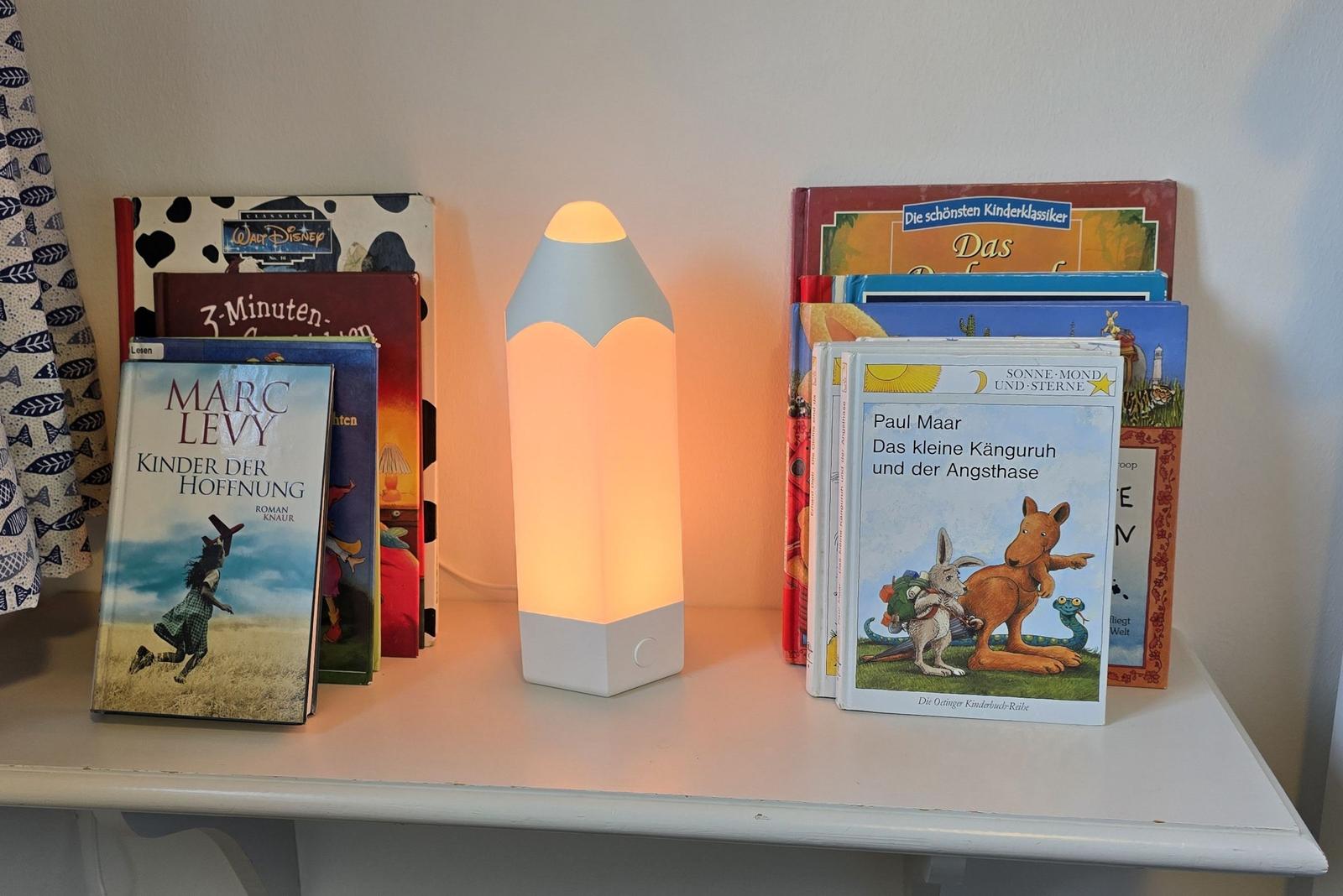 Regal mit Büchern und einer beleuchteten Bleistift-Lampe.
