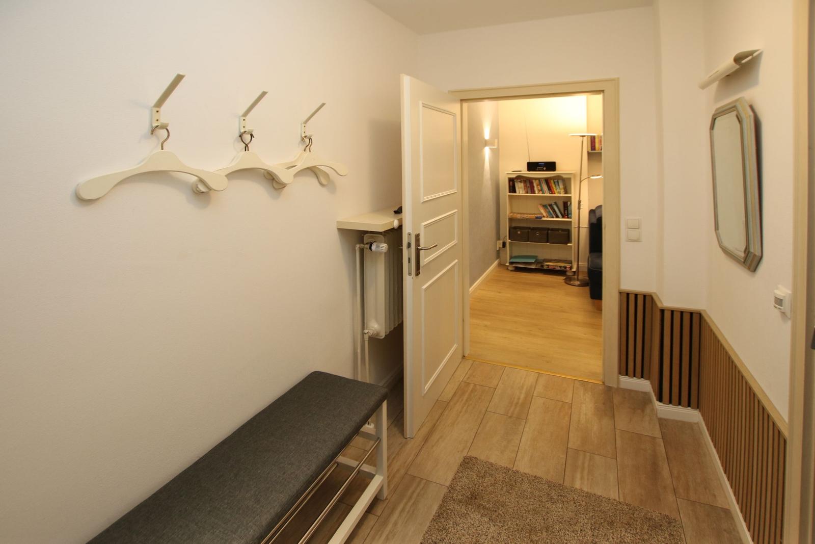 Flur mit Garderobe, Bank und Blick in Wohnzimmer mit Bücherregal.