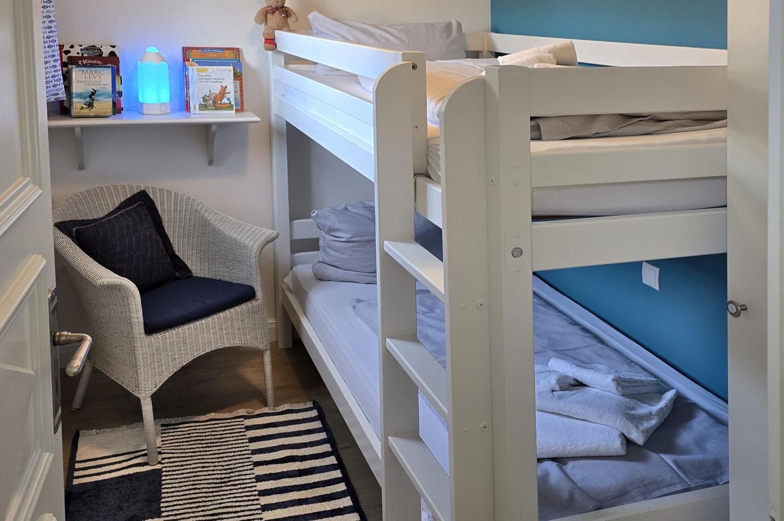 Ein Schlafzimmer mit einem weißen Doppelstockbett, einem Stuhl und einem Bücherregal.