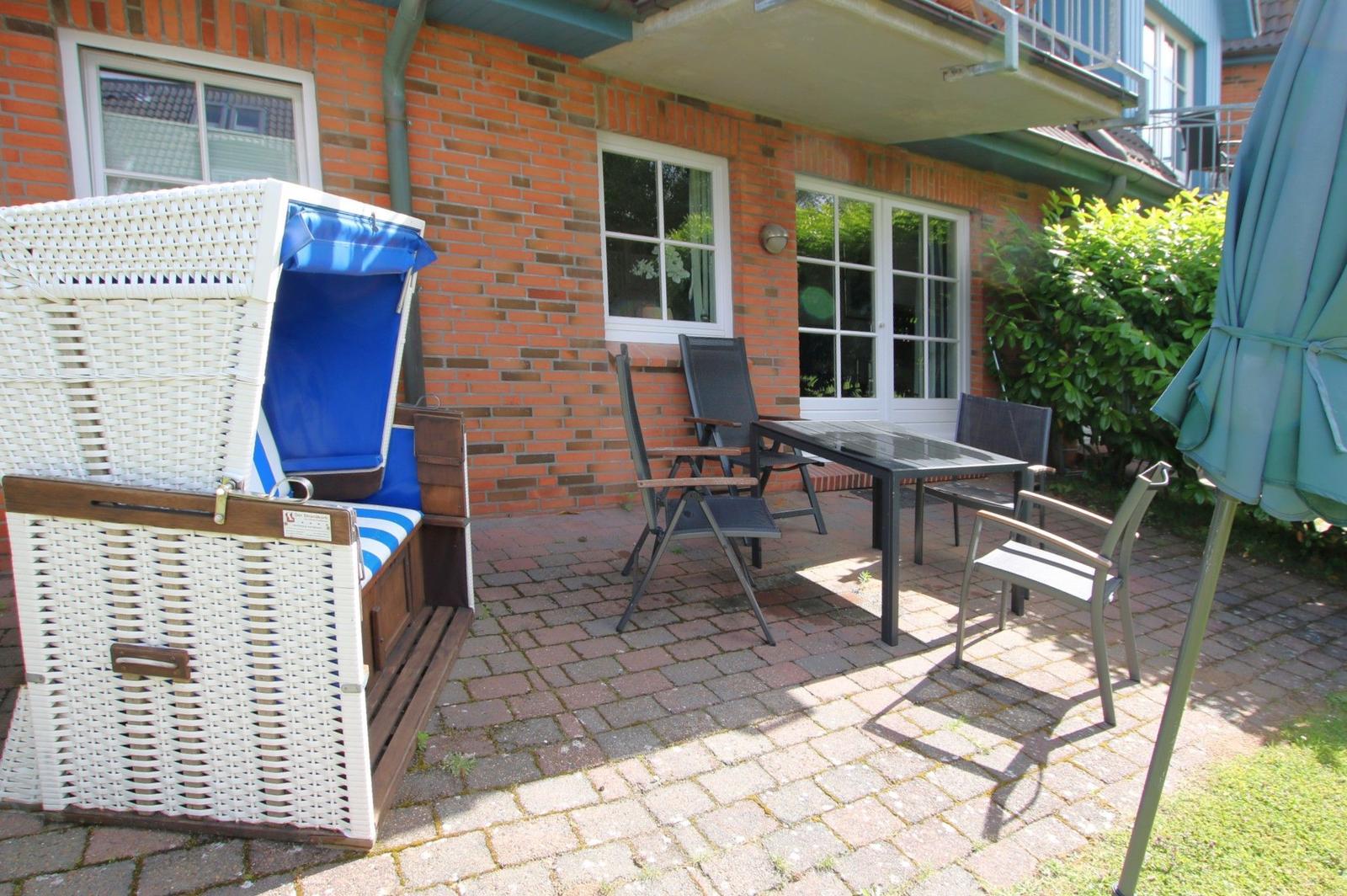 Terrasse mit Loungemöbeln, Sonnenschirm und Blick auf Hauswand.