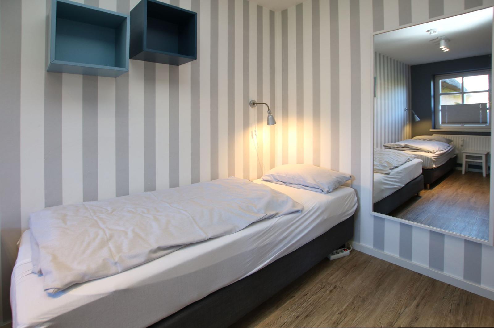 Ein Schlafzimmer mit Bett, Wandregalen und Spiegel. Wandtapete mit Streifenmuster.