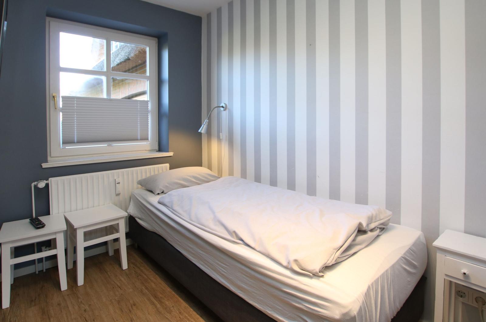 Ein Schlafzimmer mit Bett, Nachttisch und Fenster mit Jalousie.