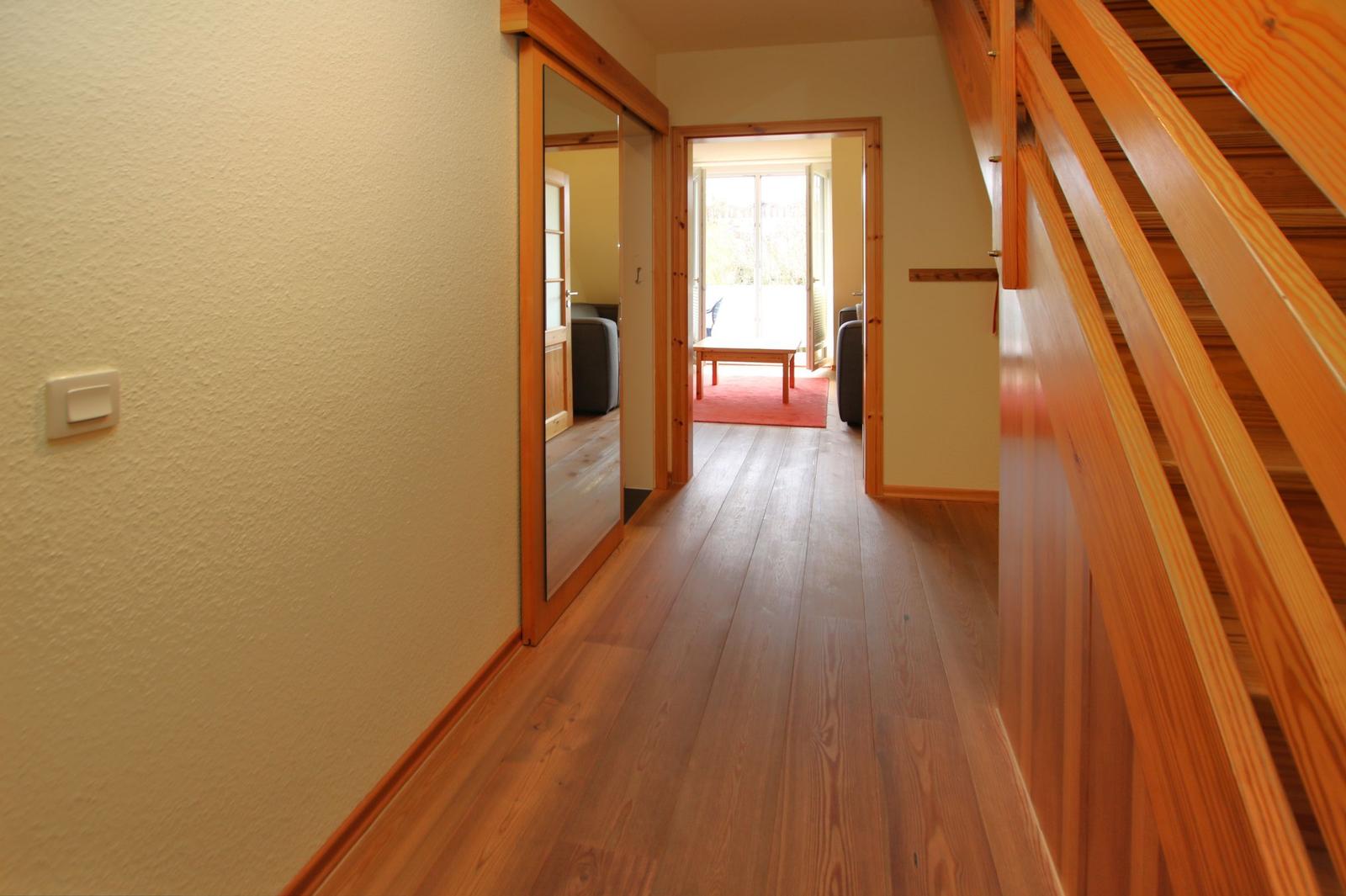Flur mit Holzboden, Treppe und Blick in Wohnzimmer mit Sofa und Tisch.