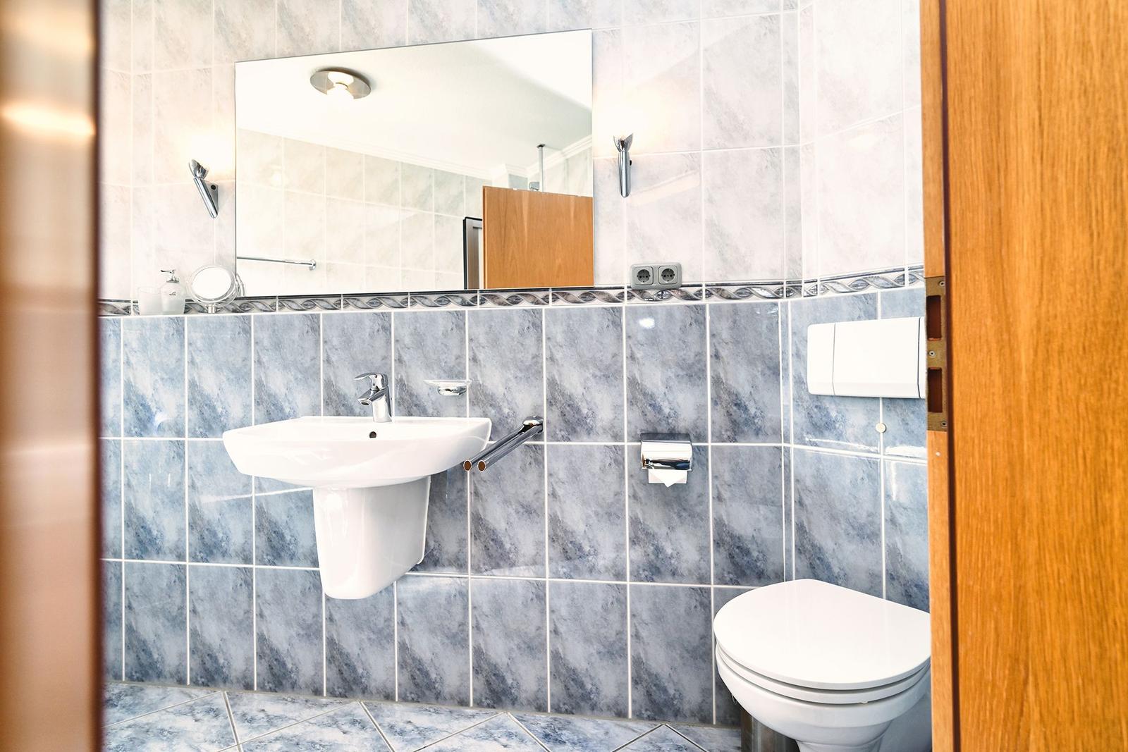 Badezimmer mit Waschbecken, Spiegel und Toilette. Wandfliesen in blau-weißem Marmoroptik.