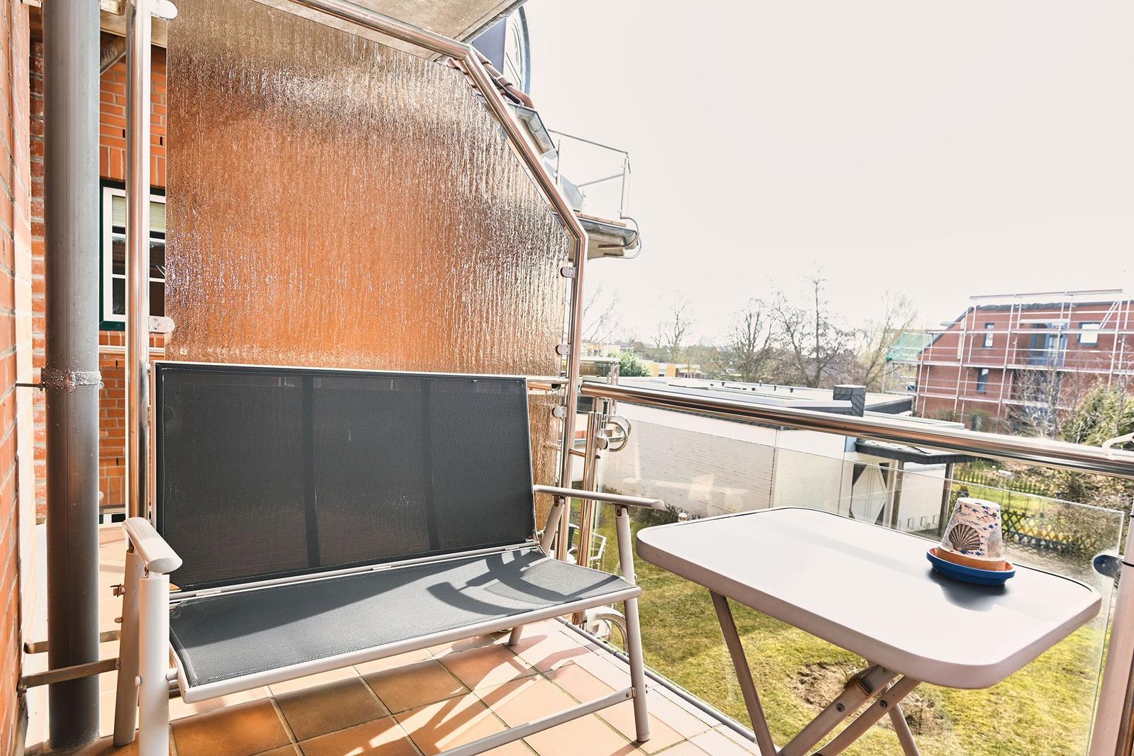 Terrasse mit Liege, Tisch und Sonnenschutz. Blick auf Wohngebiet und Grünflächen.