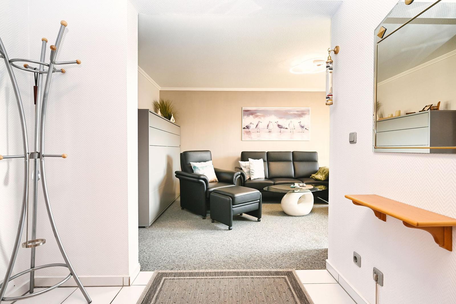 Wohnbereich mit Ledersofa, Sessel und Glas-Tisch. Spiegel und Garderobe im Eingangsbereich.