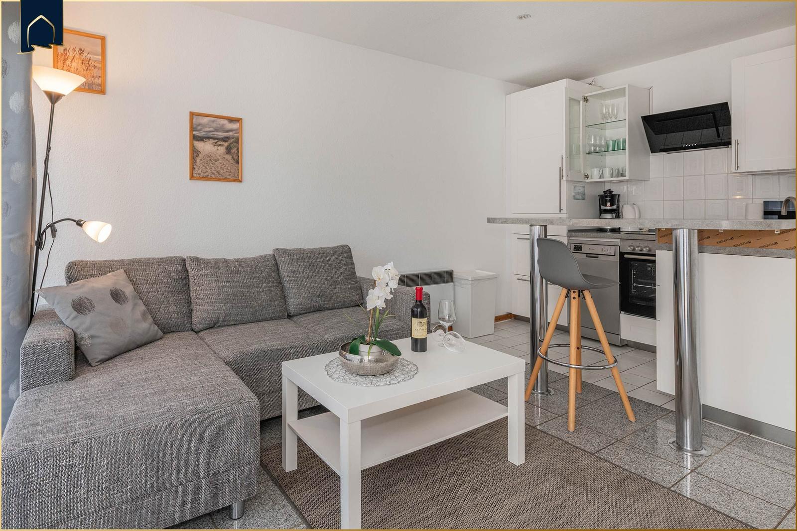 Wohnbereich mit Sofa, Tisch und Küchenzeile mit Hochstuhl.
