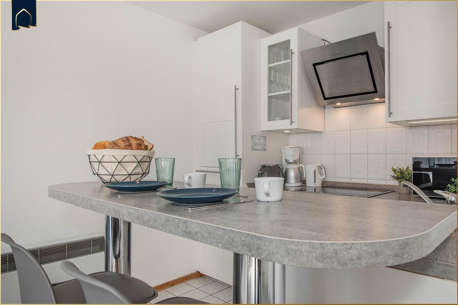 Küche mit Arbeitsfläche, Kühlschrank, Dunstabzug und Essbereich mit Tisch und Stühlen.