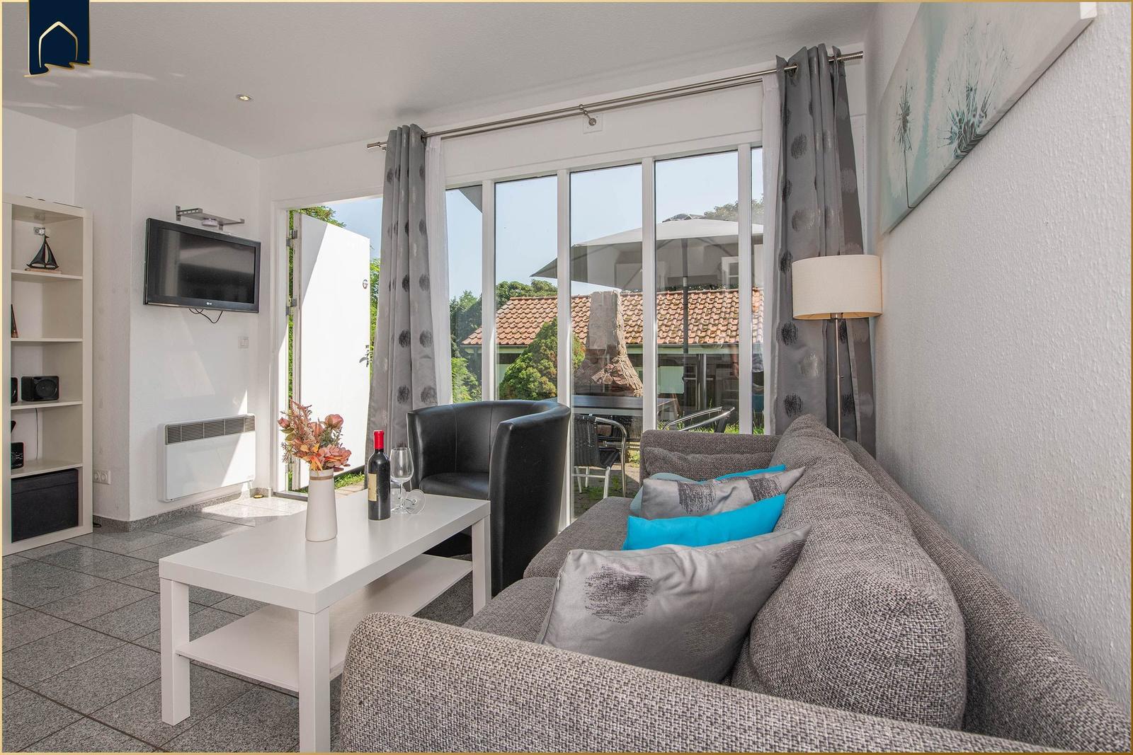 Wohnzimmer mit Sofa, Couchtisch und TV. Durchgehende Glasfront zur Terrasse.