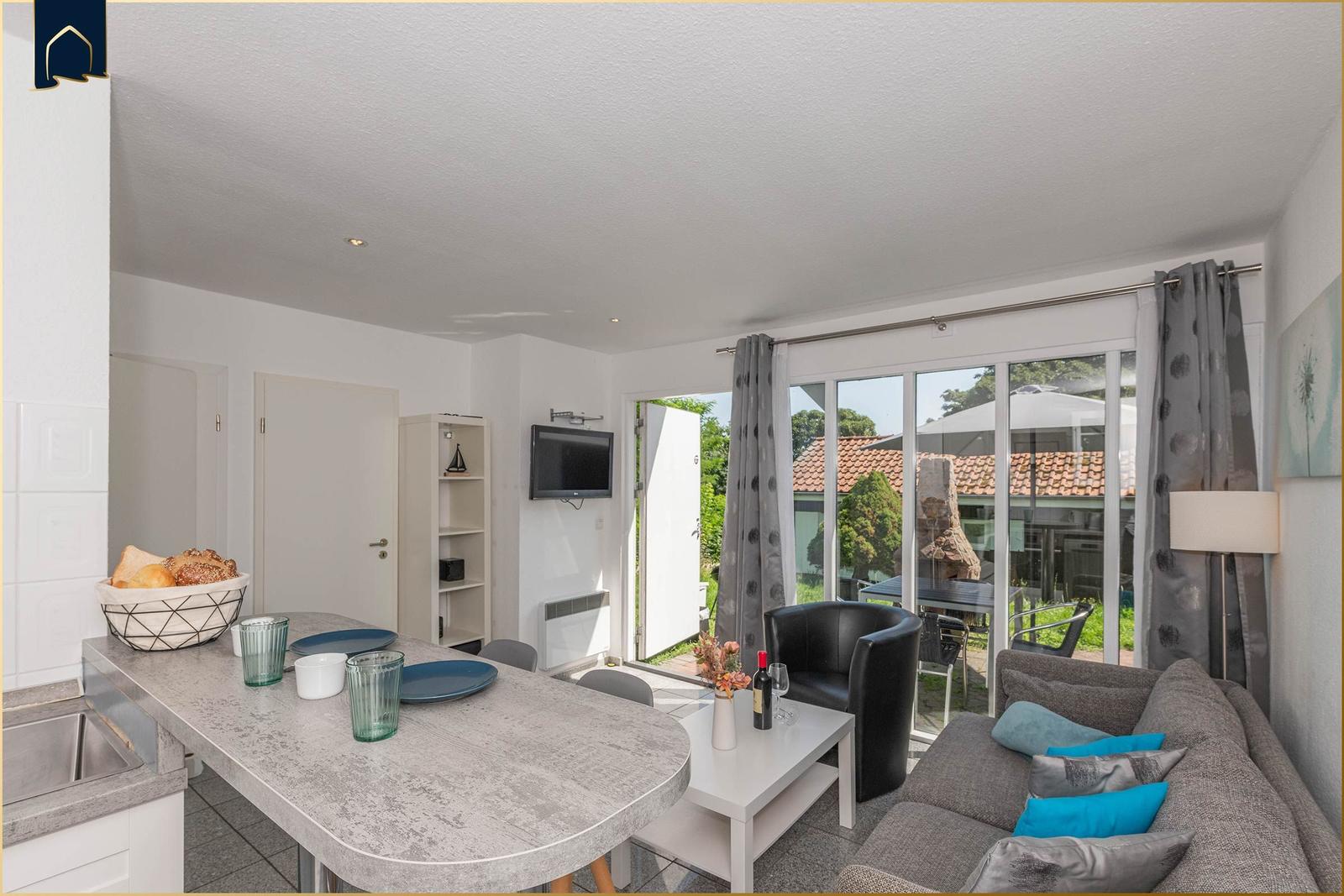 Wohnküche mit Essbereich, Sofa, Fernseher und Blick auf Garten.