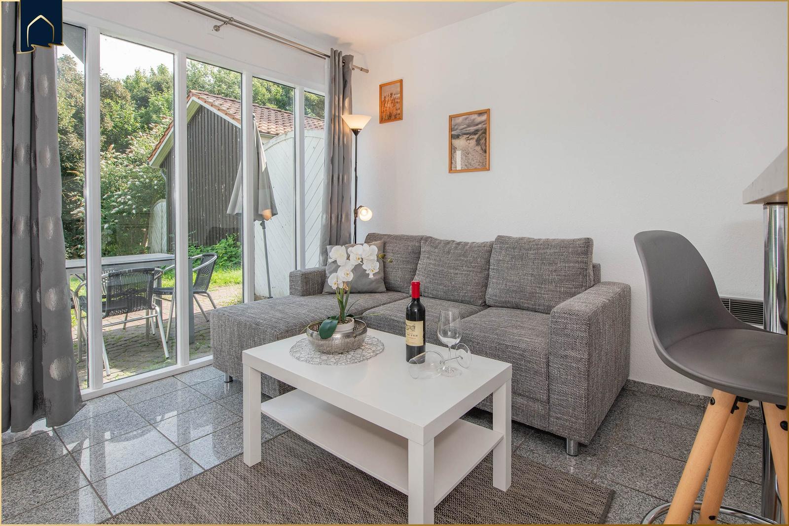 Wohnzimmer mit grauem Sofa, weißem Tisch und Blick auf die Terrasse.