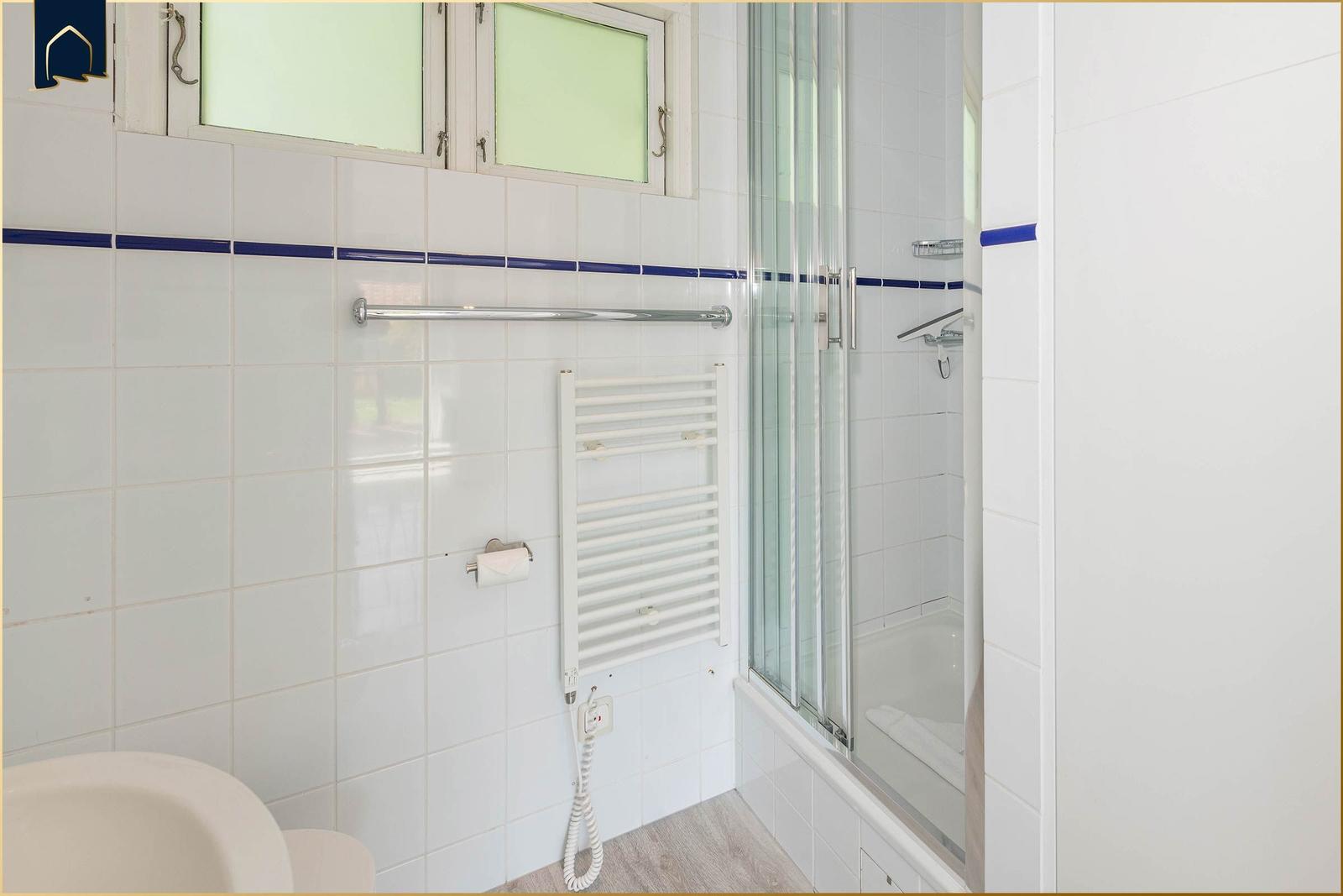 Badezimmer mit Dusche, Heizkörper und Fenster. Wandfliesen und Holzboden.